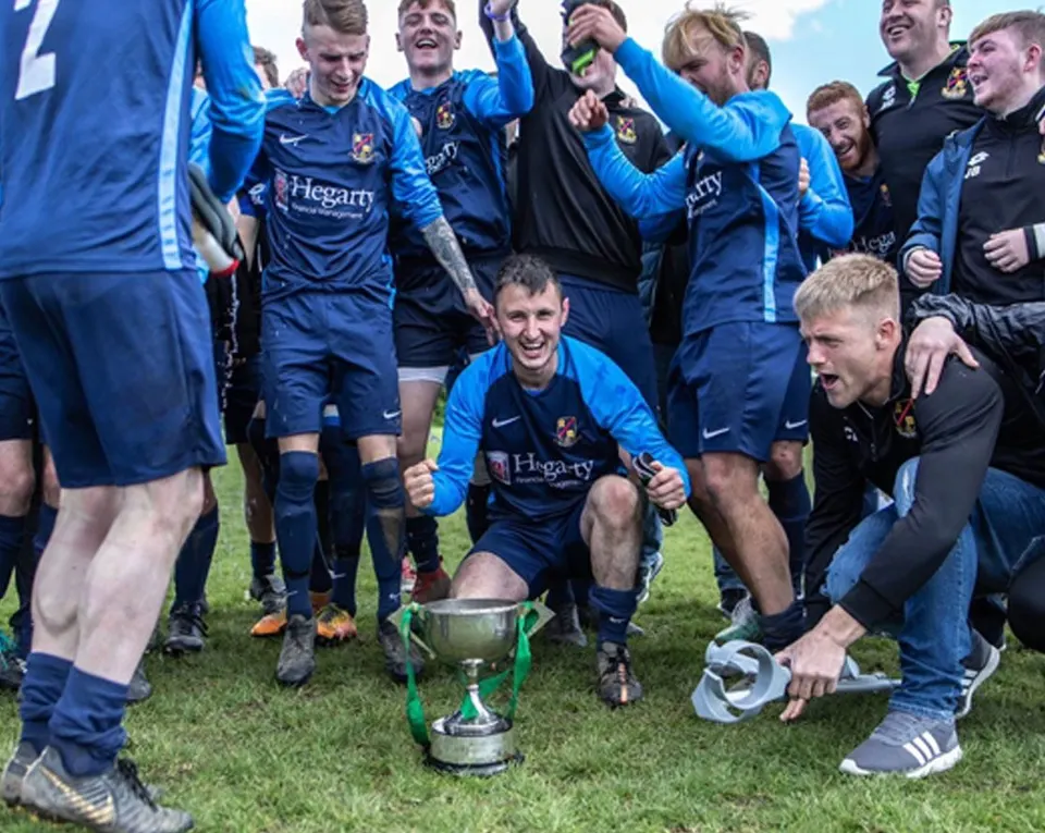 Rosemount Senior Men's team surrounding a trophy. They are all dressed in blue strip and celebrating a win.celebrating